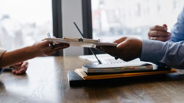 Hands pass a clipboard across a desk during a job interview.