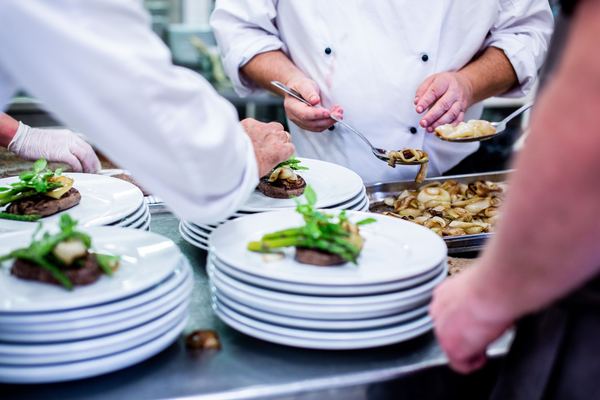 Chefs' hands plate dishes on a busy restaurant kitchen line.