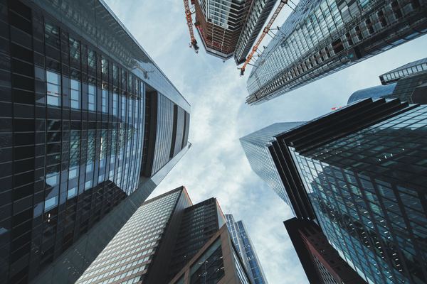 Glass office towers seen from street level, pointing into a cloudy sky.