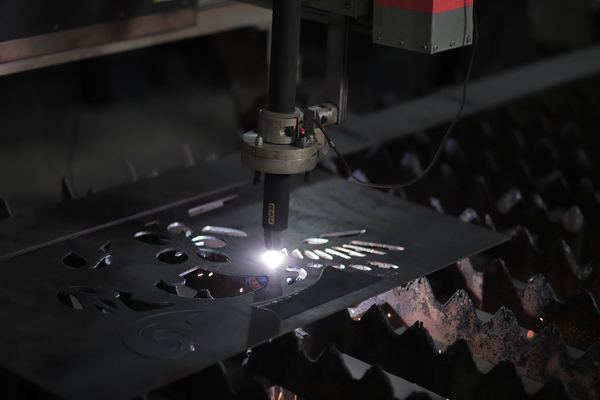 A plasma cutter slices shapes out of a thick steel sheet in the dark.