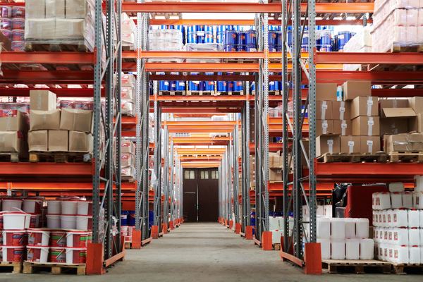 Tall orange pallet racks full of boxes and buckets line a warehouse aisle.