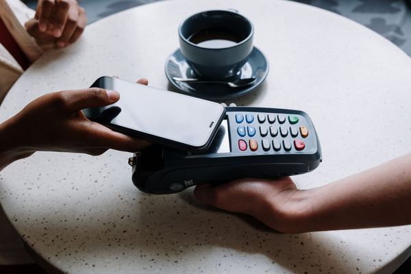 A phone is held over a card terminal on a cafe table to pay.