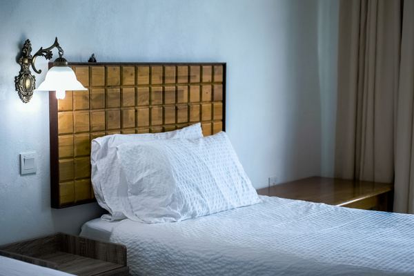 A neat hotel bed with white pillows under a wall lamp.