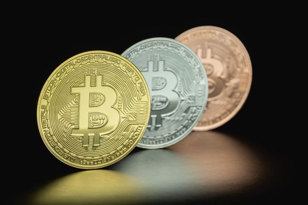Gold, silver and bronze bitcoin tokens standing in a row on black.