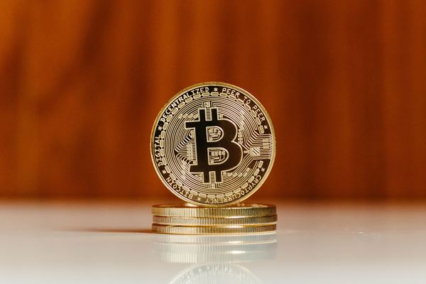 A single gold bitcoin token balanced on a short stack of coins.