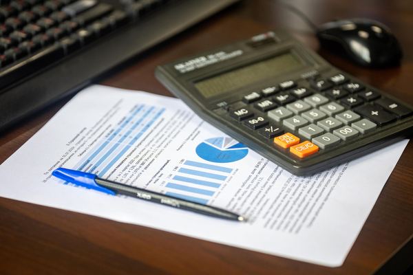 A calculator and pen rest on a printed financial report with charts.