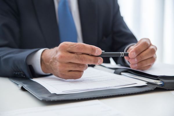 A man in a suit holds a pen over documents in a leather folder.