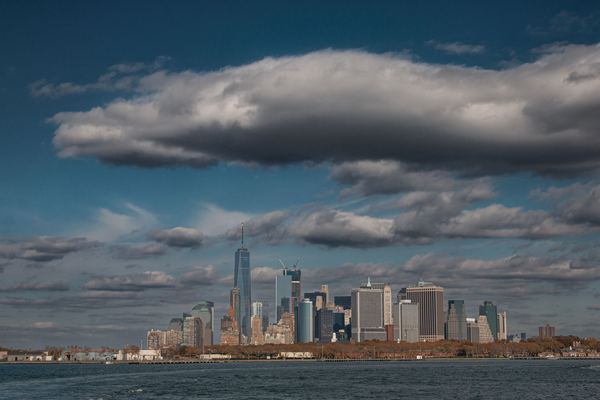 The Lower Manhattan skyline under heavy clouds, seen from the harbor.
