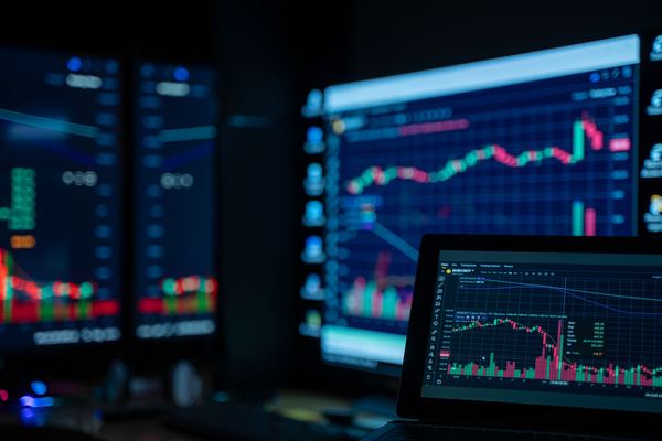 Trading monitors glow with price charts in a dark room.