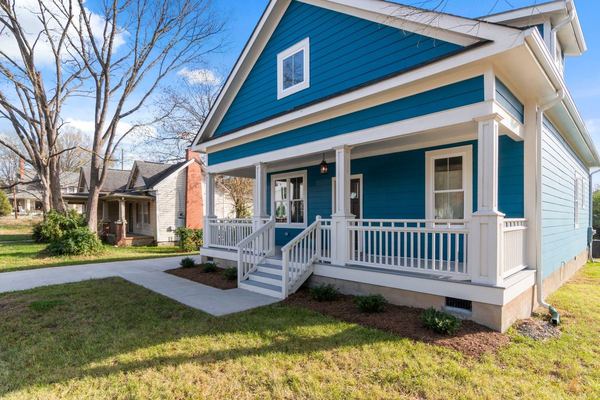 A blue craftsman house with a white front porch on a tree-lined lot