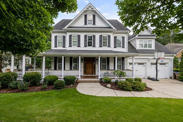 A large white colonial house with a wraparound porch and green lawn