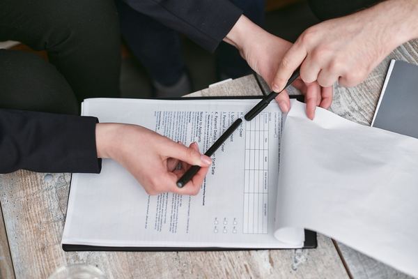Two people's hands over a clipboard as one signs loan paperwork