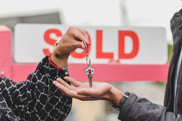House keys handed over in front of a red Sold sign
