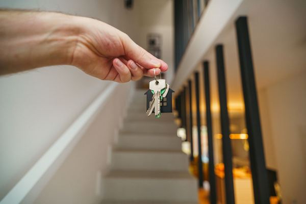 A hand holding a set of house keys beside a staircase