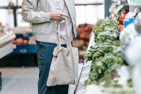 A shopper with a cloth tote bag reaching for produce, face not shown