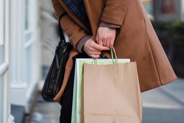 A shopper holding paper shopping bags on a city sidewalk