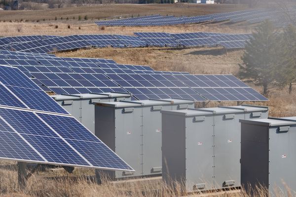Grey battery and inverter cabinets beside rows of solar panels