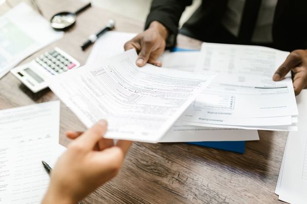 Two people passing tax documents across a desk, hands only