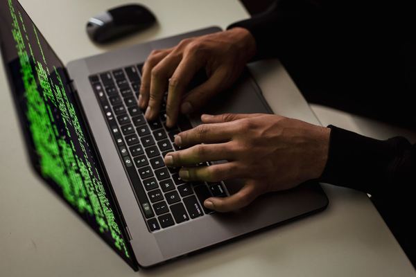 Hands typing on a laptop with green code on the screen