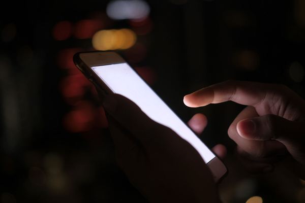 Hand tapping a glowing smartphone screen in the dark