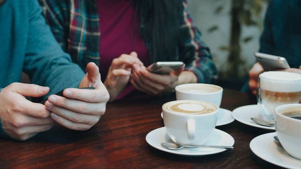 Friends at a cafe table looking at their phones beside cups of coffee
