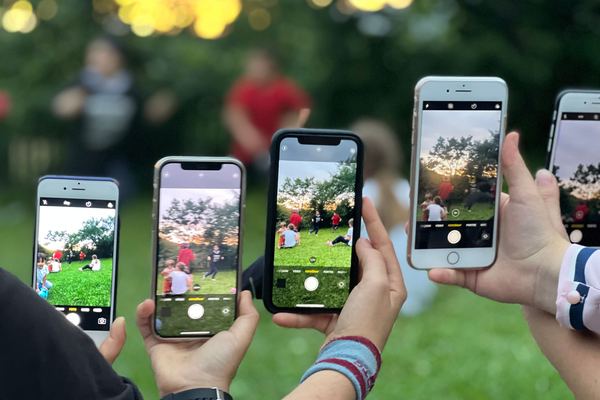 Several people holding up phones to film an outdoor event