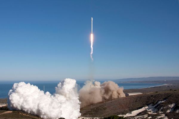 Rocket climbing into a clear blue sky above a coastal launch pad